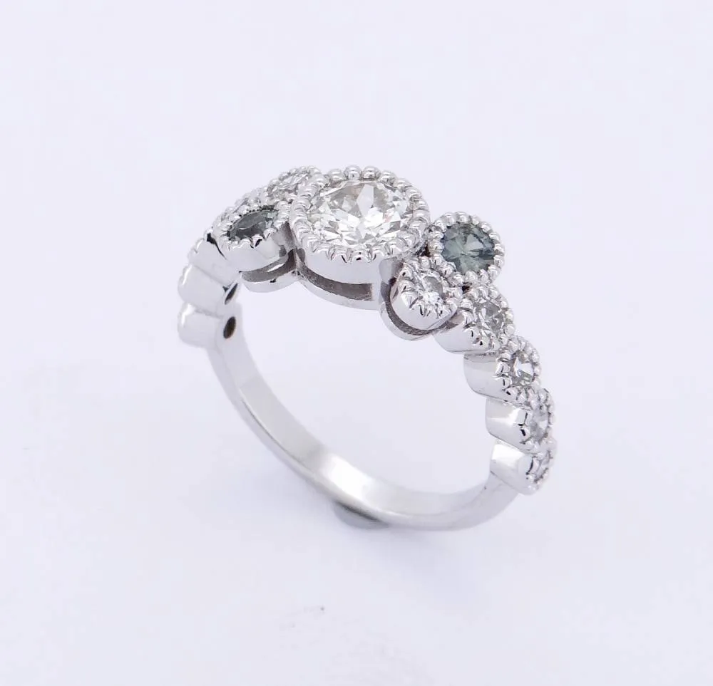 Bague en or blanc 18 carats ornée d’un saphir vert central et de diamants, création joaillière artisanale.