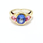 bague moderne avec une tanzanite au centre taille coussin de 3 carats et deux saphirs rose poire sur les cotés monture or jaune