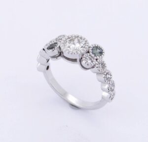 Bague en or blanc 18 carats ornée d’un saphir vert central et de diamants, création joaillière artisanale.