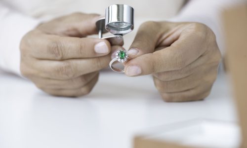 expertise d'un bijou en or blanc et une émeraude dans les mains du joaillier avec sa loupe